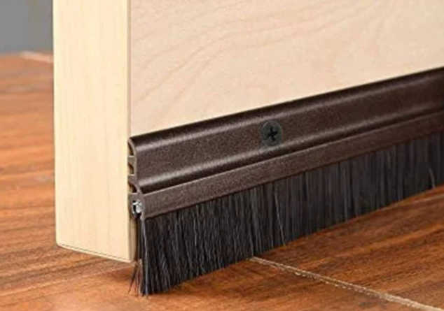 A light brown door with a dark brown brush draft stopper attached to the bottom.
