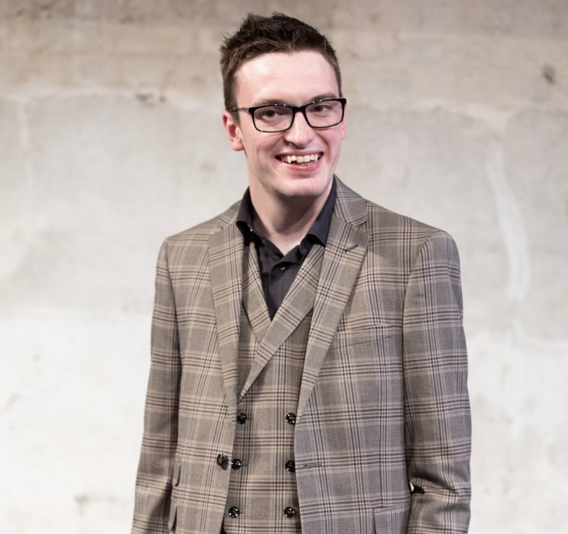 Ciaran is a white male wearing glasses and a checked suit. Ciaran is looking to camera.