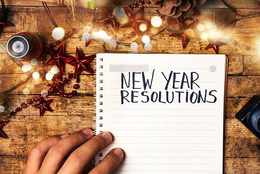 A notepad that states "New Years Resolution" at the top. On a wooden desk with Christmas decorations around it.