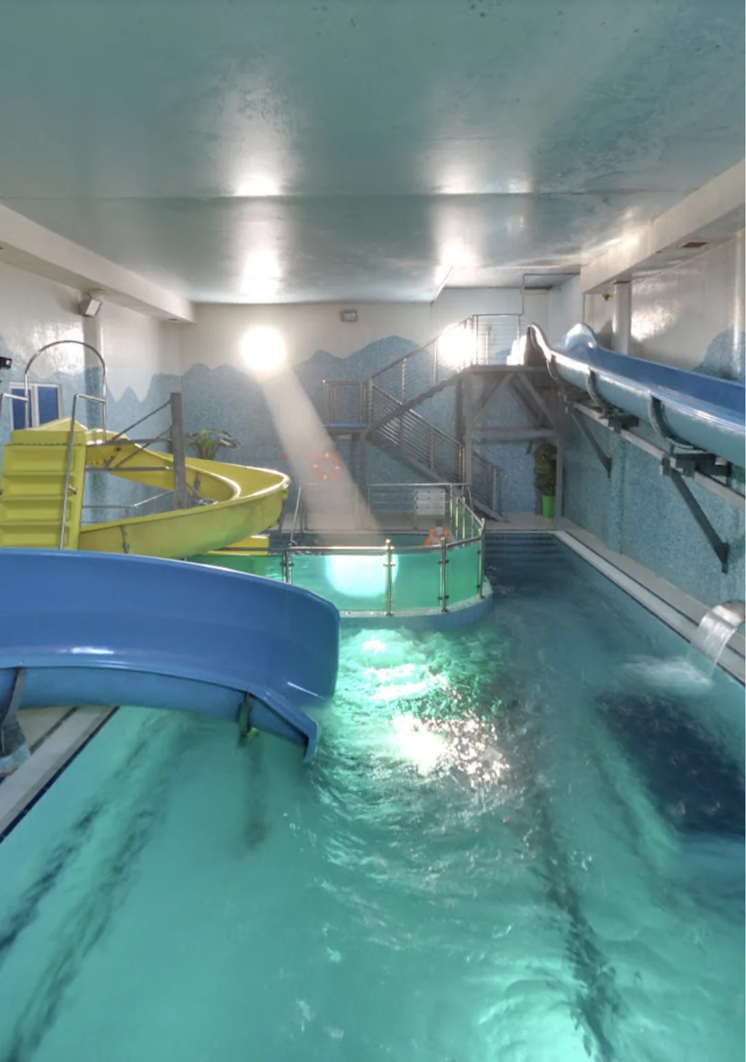A pool with 2 blue slides and 1 yellow slide