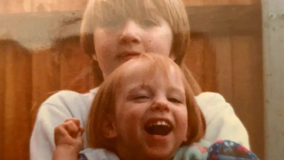 An old photo of Sarah and Vicky. They are both children. They are looking and smiling at the camera.