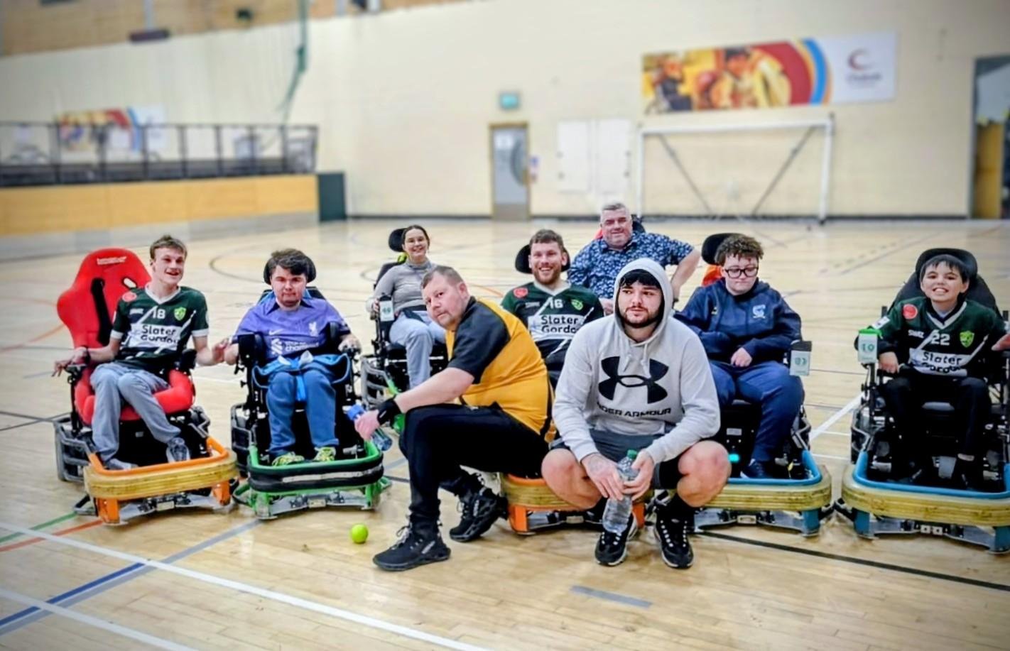 7 people in power wheelchairs look in the camera. Two people sit on the floor looking in the camera