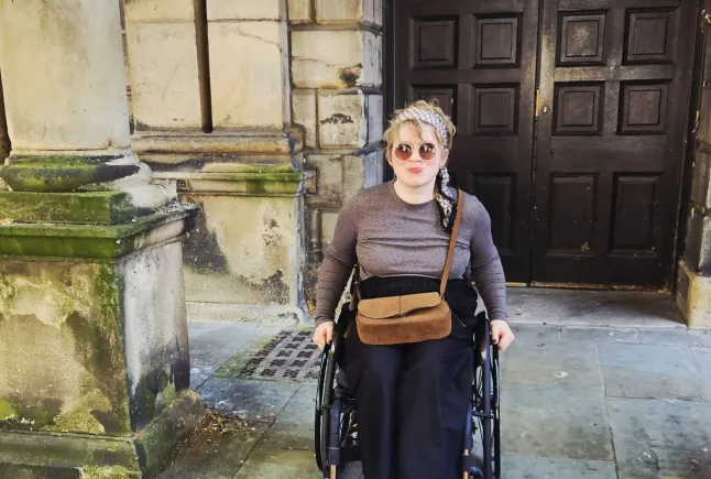 Melissa Parker in her wheelchair, in front of an old building with some large wooden double doors and stone pillars