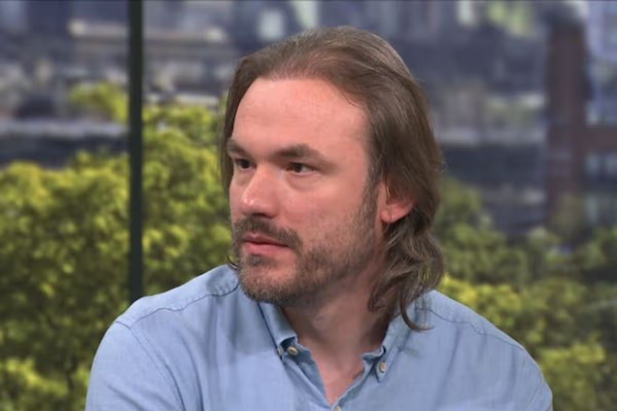 A screenshot of James sitting on the This Morning sofa. He has long brown hair, and a beard