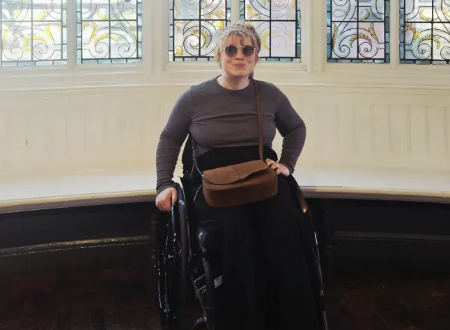 Melissa Parker in her wheelchair in front of some stained glass windows, wearing sunglasses