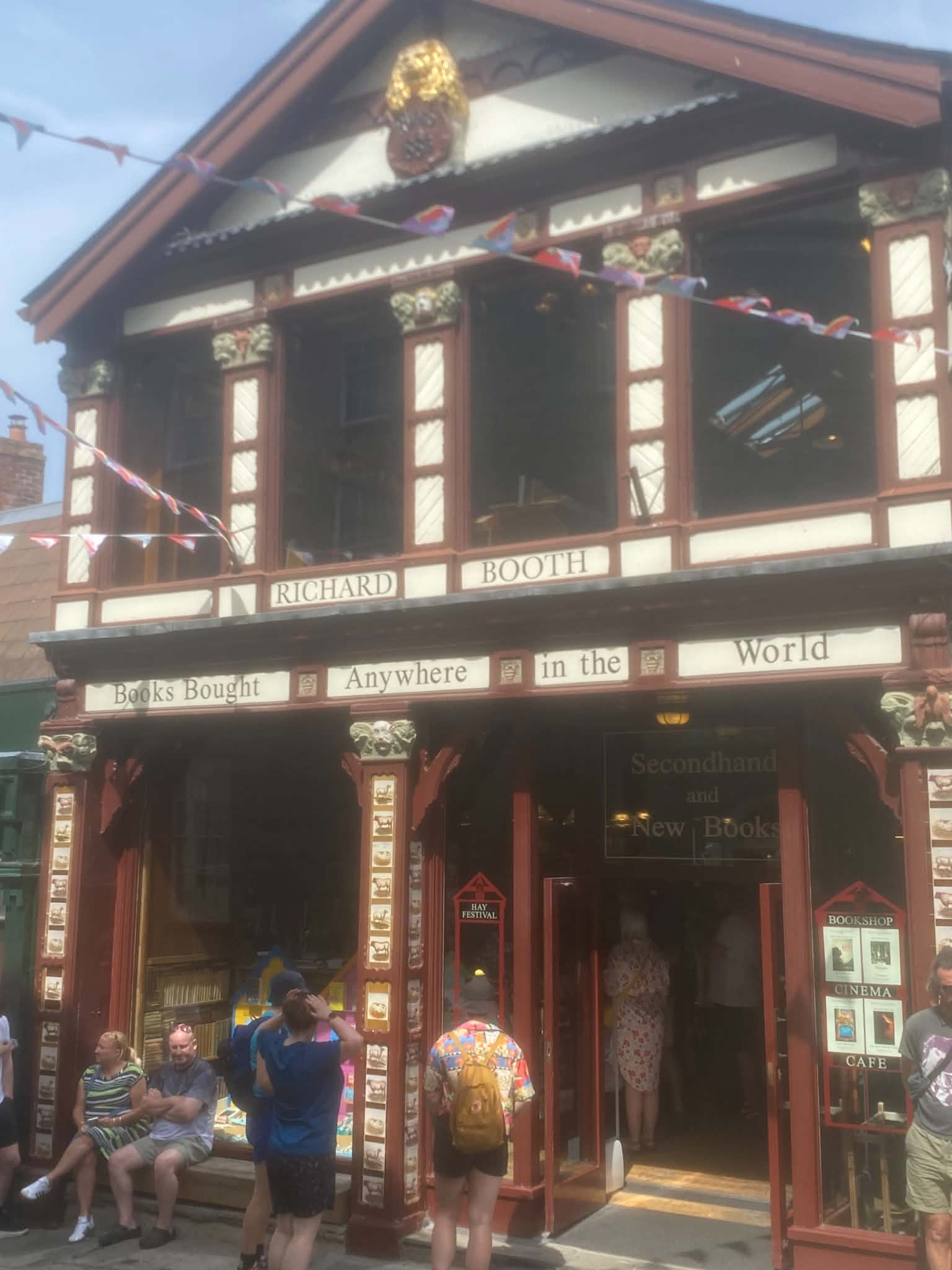 The wooden facade of a multi-story building featuring classical decorative columns and festive string banners hanging outside, with people standing near the front entrance.