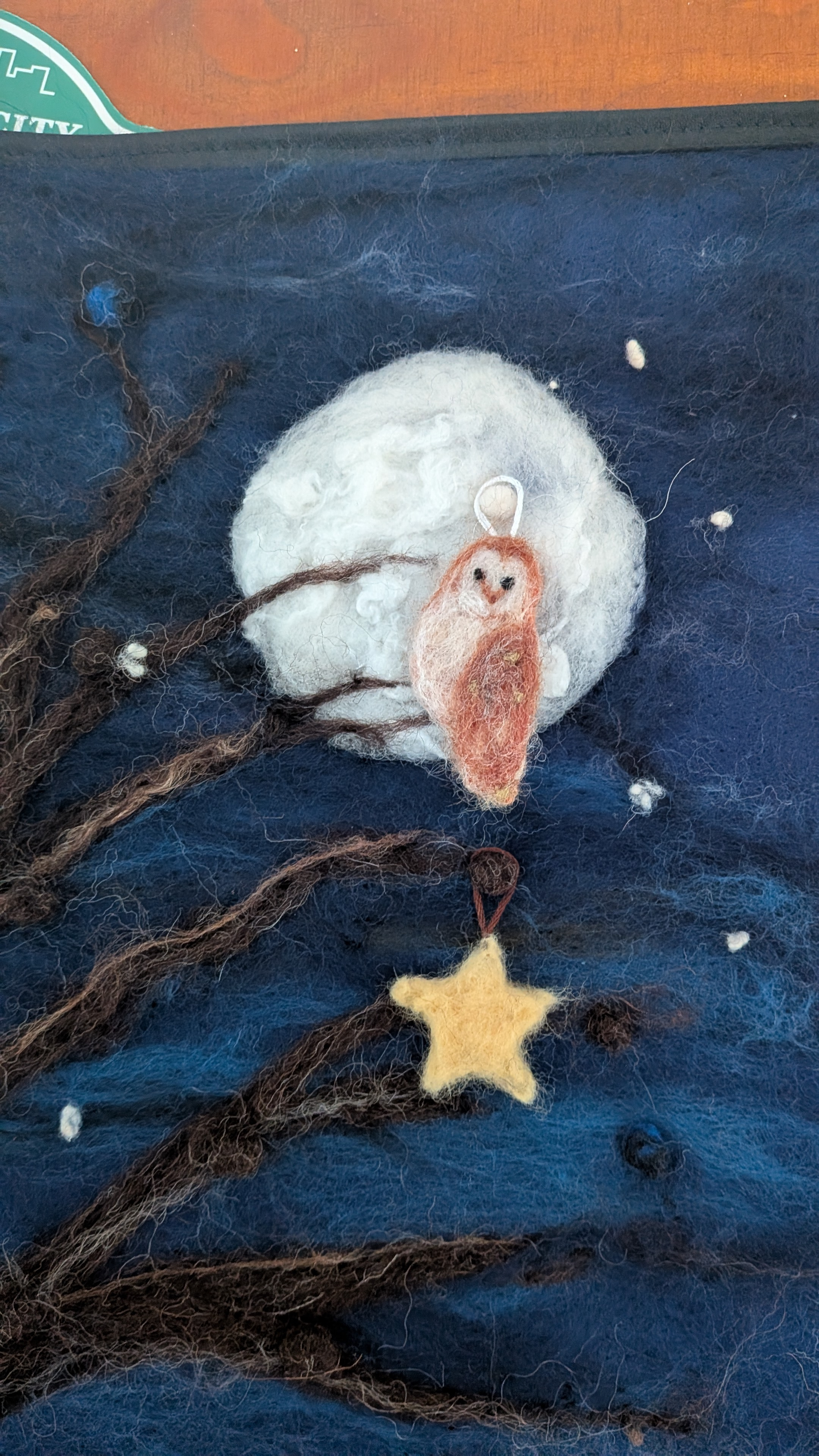 a needle felted barn owl against a white full moon. A yellow star hangs below it