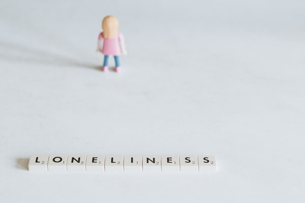 small toy figure standing alone in front of scrabble tiles that spell out the word loneliness