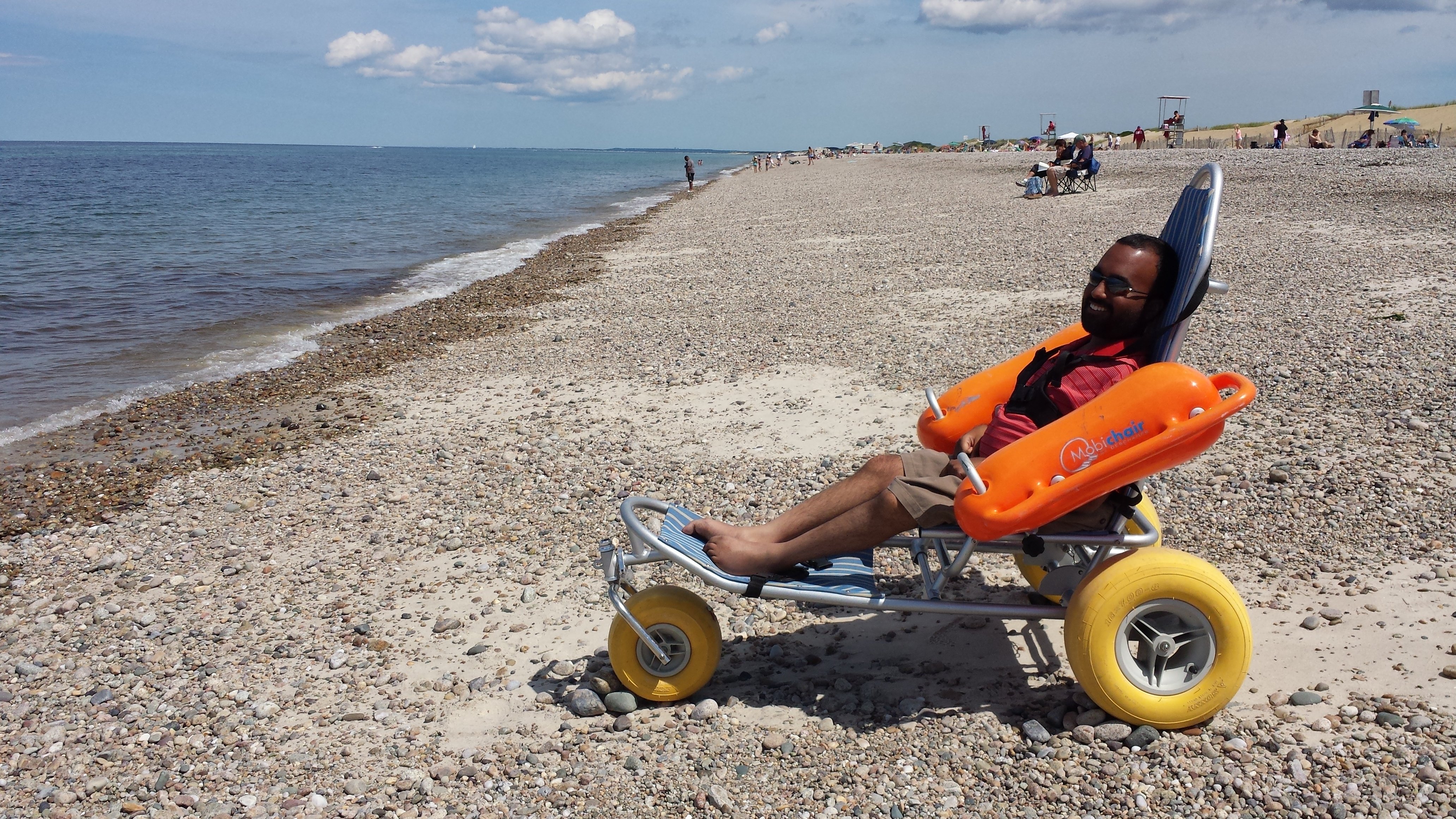 Man sitting on an adapted wheelchair on the beach next to the sea