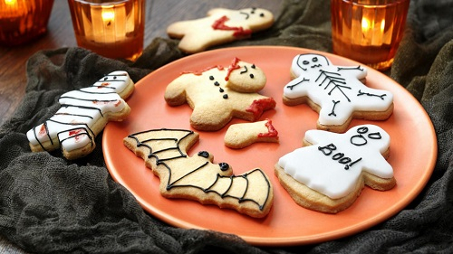 Orange plate covered in halloween inspired cookies including a bat skeleton and ghost