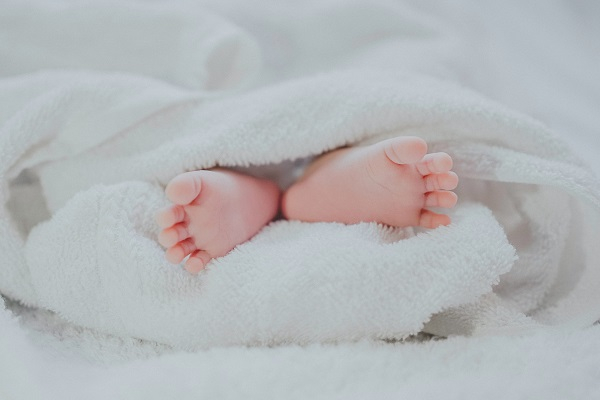 A photo showing a pair of babys feet sticking out of the bottom of a white blanket