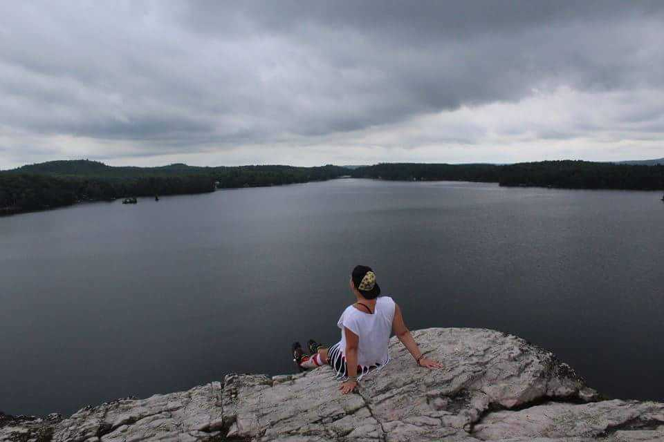 landscape image taken from behind of a girl sat on rocks and looking out over the mountains and sea in the distance