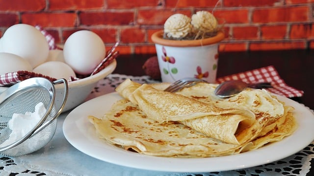 stack of pancakes on a plate with eggs behind