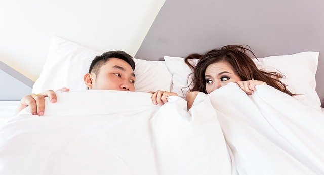 two people in bed with white sheets pulled up to their chins