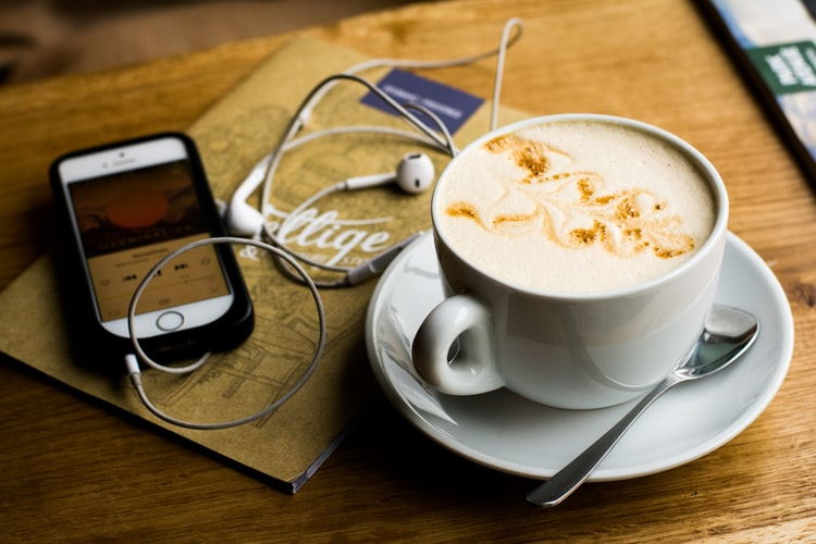 cup of coffee next to a phone with earbuds coming out of it