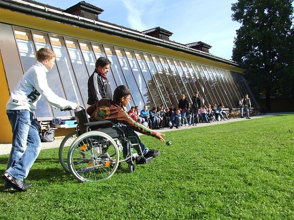 A young man in a wheelchair throwing a ball along the ground while other children watch