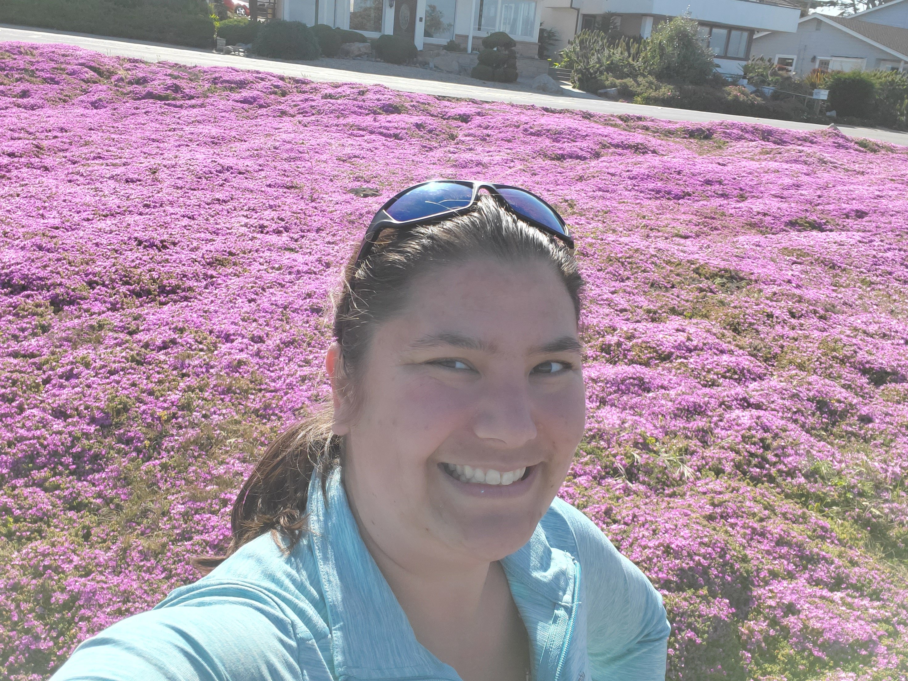 Emma's selfie - a smiling woman with brown hair and a blue jacket in front of a filed of purple flowers