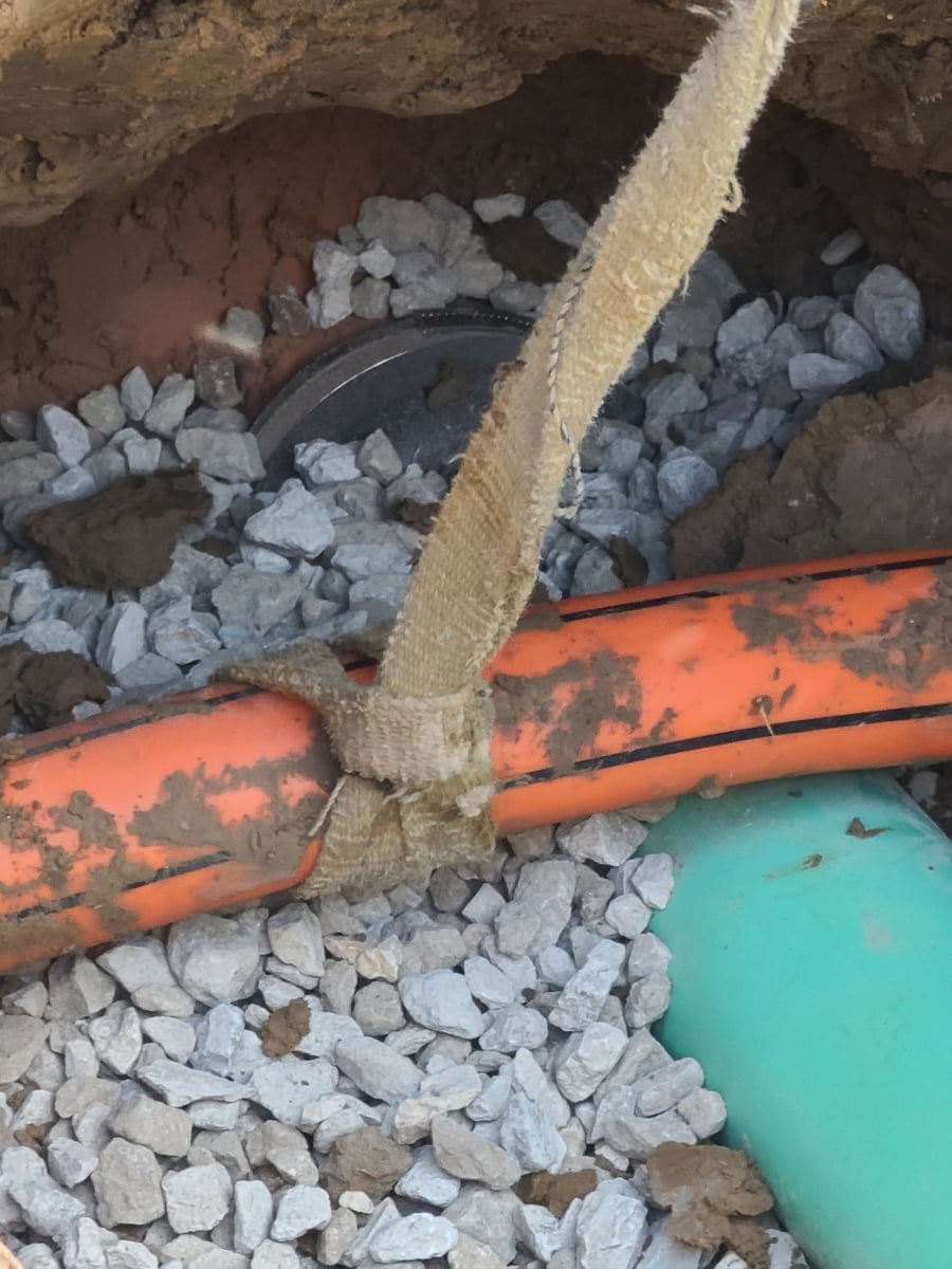 Repaired sewer pipe under orange conduit/cable